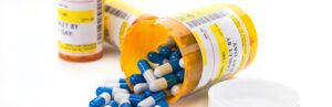 Image of a prescription bottle toppled over showing white and blue pharmaceutical drugs