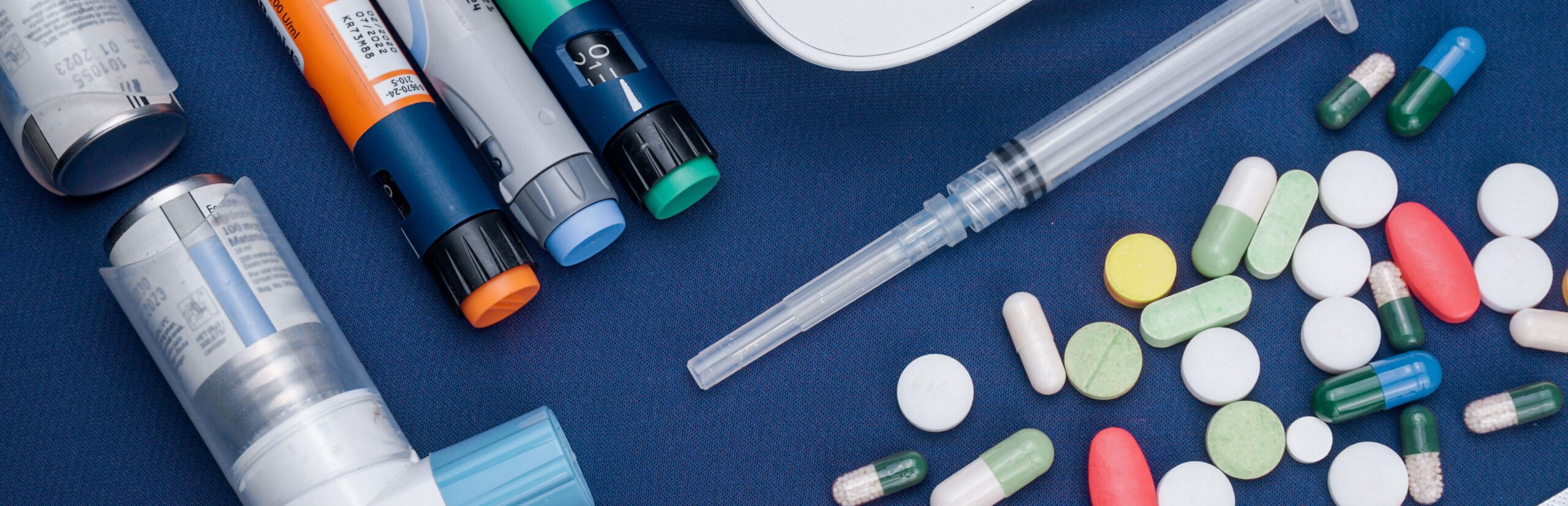 Drugs-banner Image of a prescription bottle toppled over showing white and blue pharmaceutical drugs